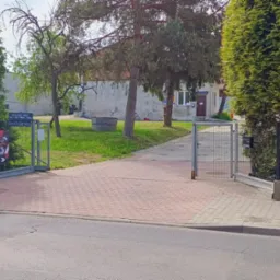 Widok na wjazd do warsztatu ShopOnService z reklamą wulkanizacji i serwisu motocyklowego, z budynkiem w tle. Otwarta brama wjazdowa.