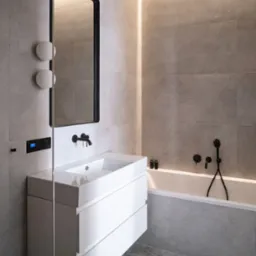 Nowoczesna łazienka w szarościach z białym blatem umywalki i czarną armaturą. Podświetlenie LED wzdłuż wanny dodaje subtelnego akcentu.