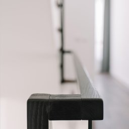 FILIP RAUPUK ARCHITEKTURA - Detal nowoczesnej balustrady schodowej z ciemnego drewna i szkła, minimalistyczny design, jasne wnętrze, neutralne tło,  widok z bliska na fragment poręczy.