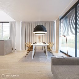 FILIP RAUPUK ARCHITEKTURA - Jasne wnętrze jadalni z dużym oknem i widokiem na zieleń. Biały stół otoczony drewnianymi krzesłami, nad nim czarna lampa. Minimalistyczny design, parkiet na podłodze.