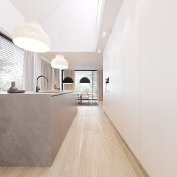 FILIP RAUPUK ARCHITEKTURA - Minimalistyczna kuchnia z wyspą i drewnianą podłogą, oświetlona lampami wiszącymi. Widok na jadalnię przez okno z żaluzjami. Białe szafki na ścianie.