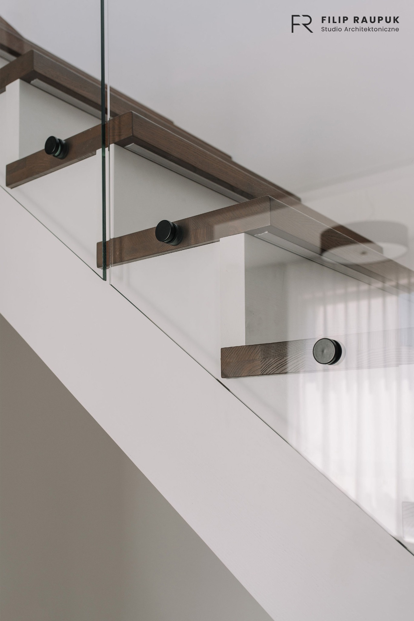 Nowoczesne schody z drewnianymi stopniami i szklaną balustradą, mocowane za pomocą czarnych uchwytów. Minimalistyczny design i jasna kolorystyka wnętrza.