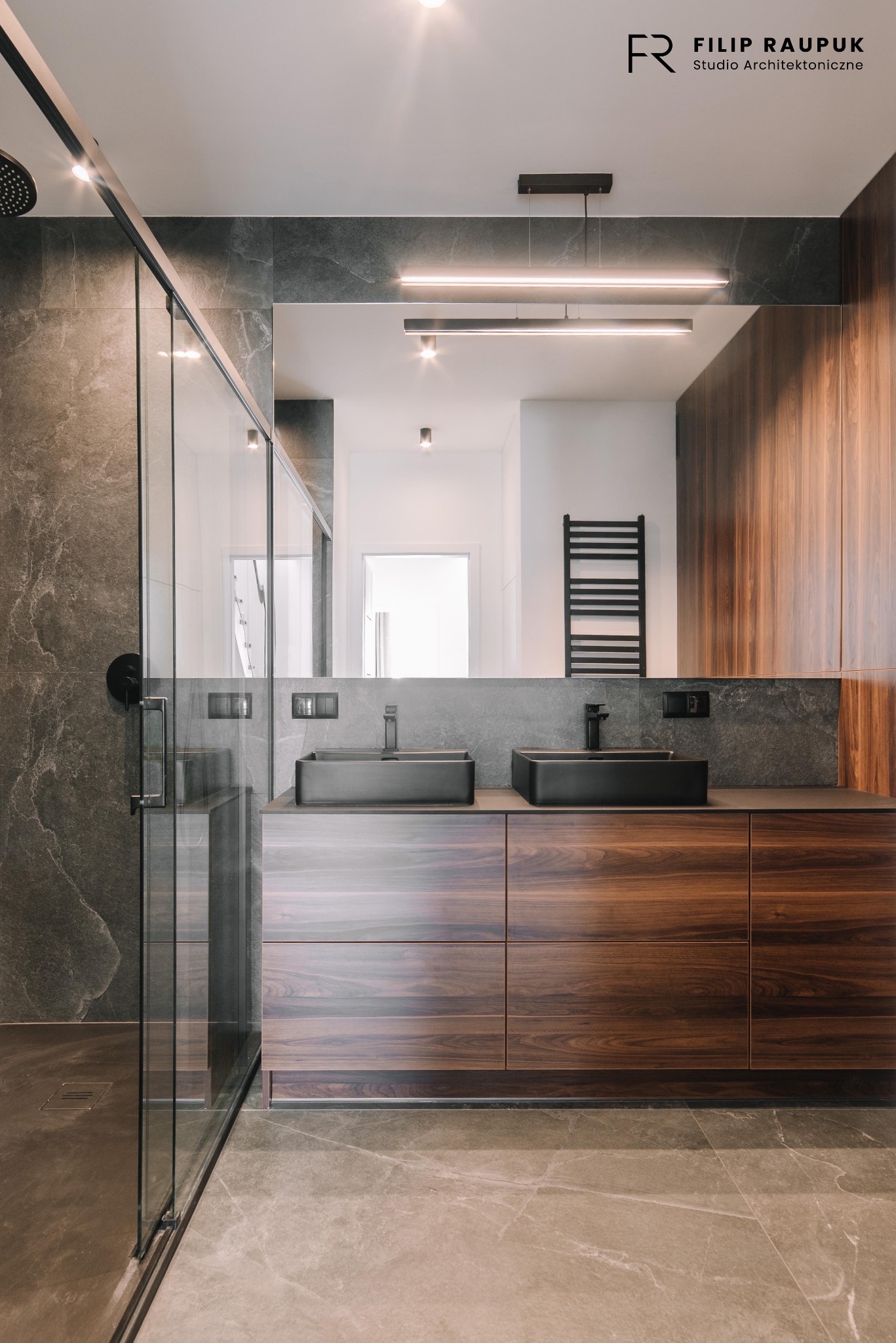 Nowoczesna łazienka z kabiną prysznicową typu walk-in, dwiema czarnymi umywalkami nablatowymi i drewnianą szafką pod umywalką. Minimalistyczne oświetlenie.