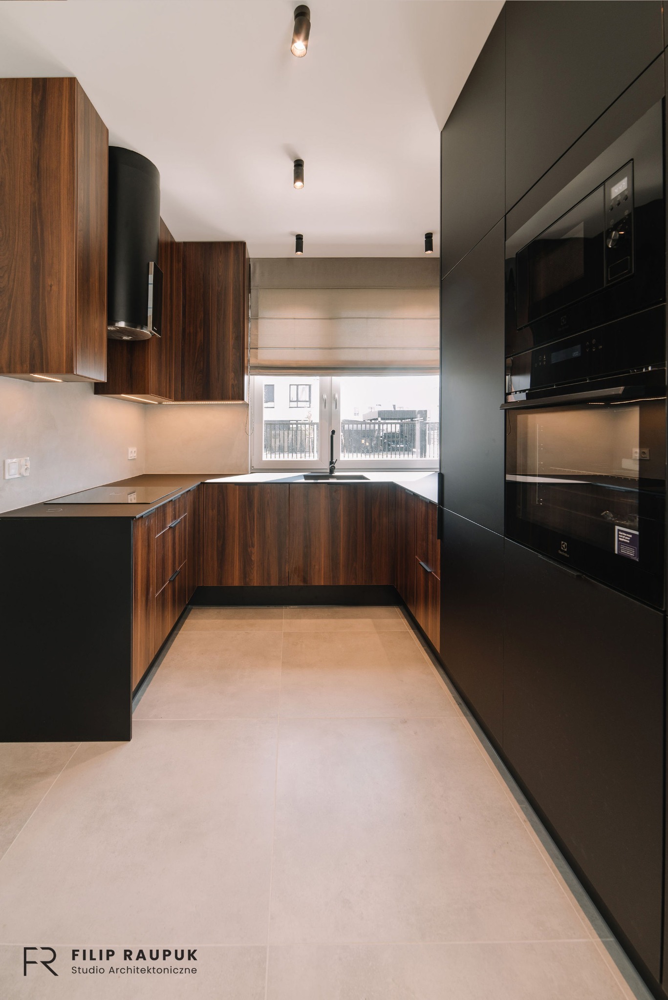 Nowoczesna kuchnia w odcieniach brązu i czerni z drewnianymi frontami szafek i sprzętem AGD w zabudowie. Minimalistyczne oświetlenie punktowe i jasna podłoga.