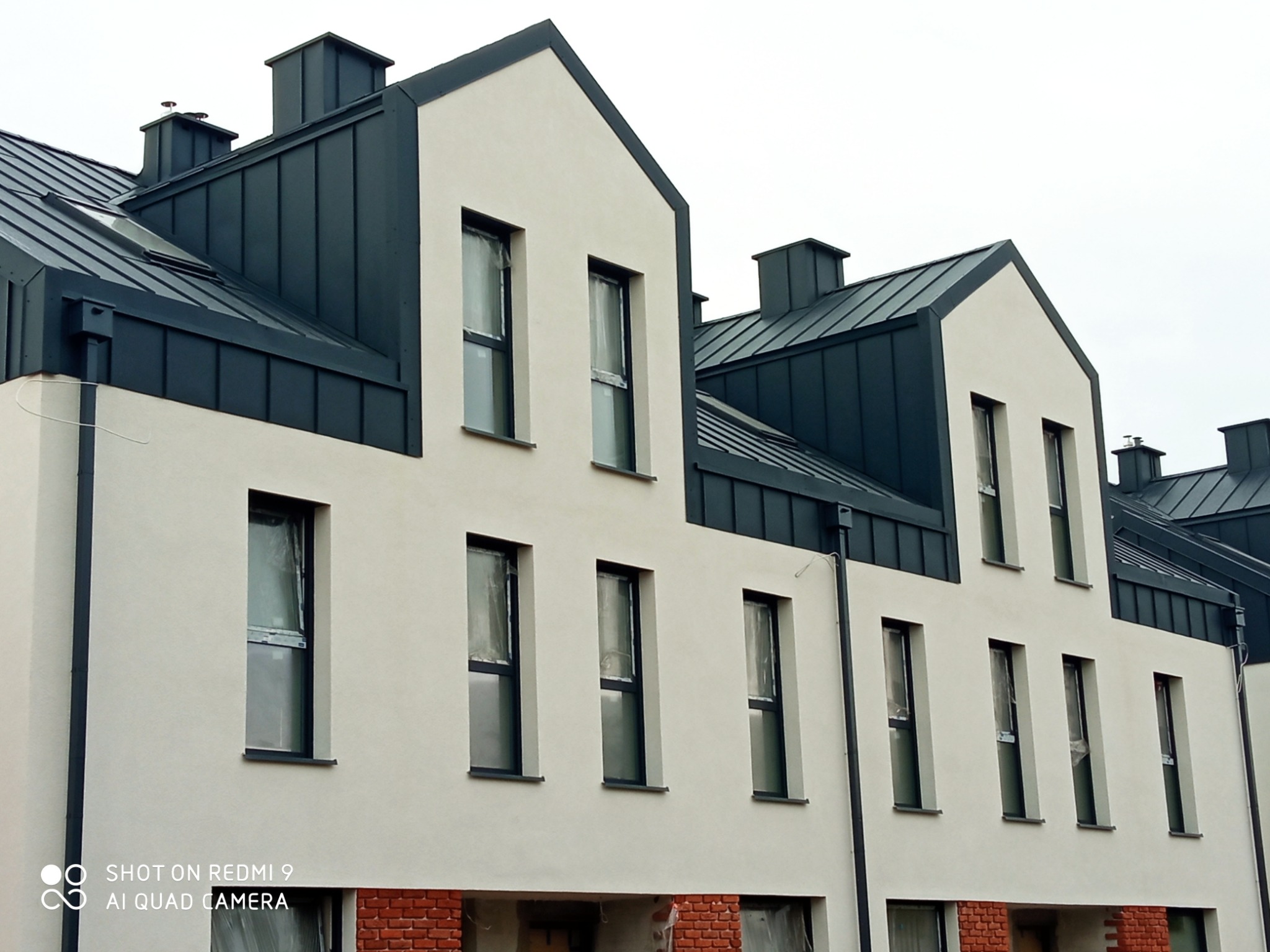 Nowoczesne budynki w Poznaniu z ciemnymi, metalowymi pokryciami dachowymi i jasną elewacją, okna zabezpieczone folią.