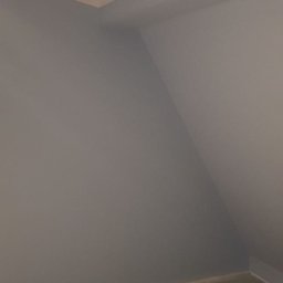 KA RENOVATION - Pomalowane na szaro poddasze ze skośnym sufitem, widoczny kabel i wiadro po farbie na podłodze.