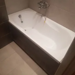 Wanna z obudową z ciemnych paneli, chromowana bateria i odpływ, beżowe płytki na ścianach i podłodze, widok z g&oacute;ry pod kątem.