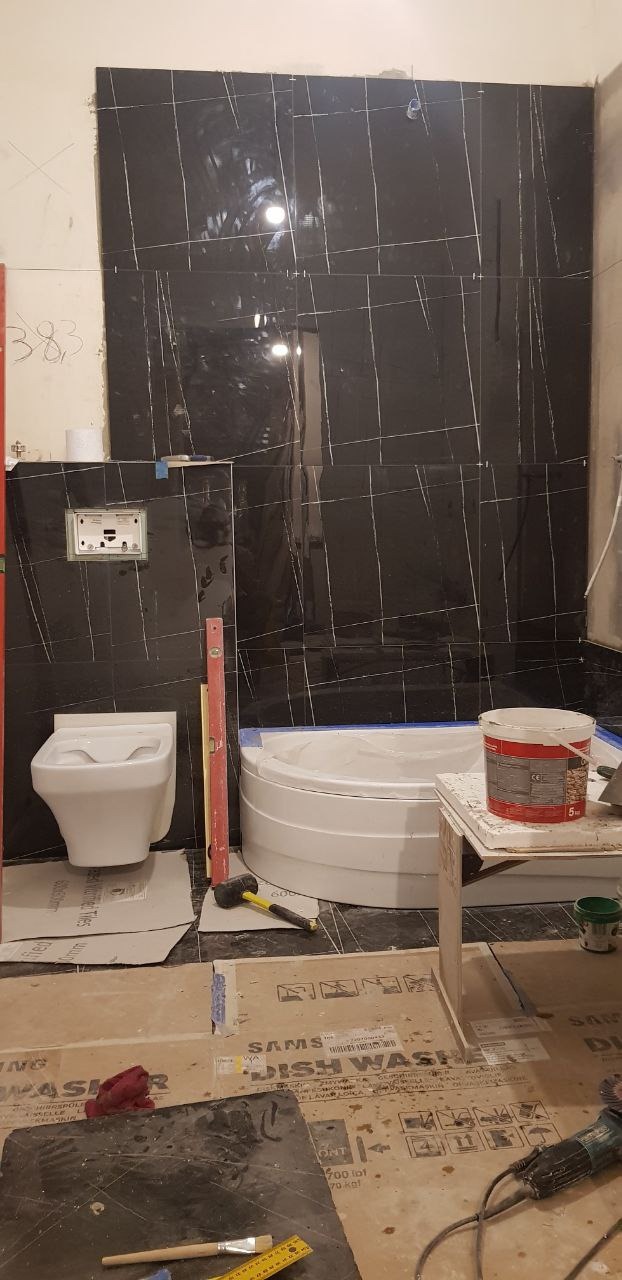 Montaż czarnych płytek imitujących marmur w łazience, widoczna wanna, miska WC, poziomica i narzędzia na podłodze zabezpieczonej kartonem.
