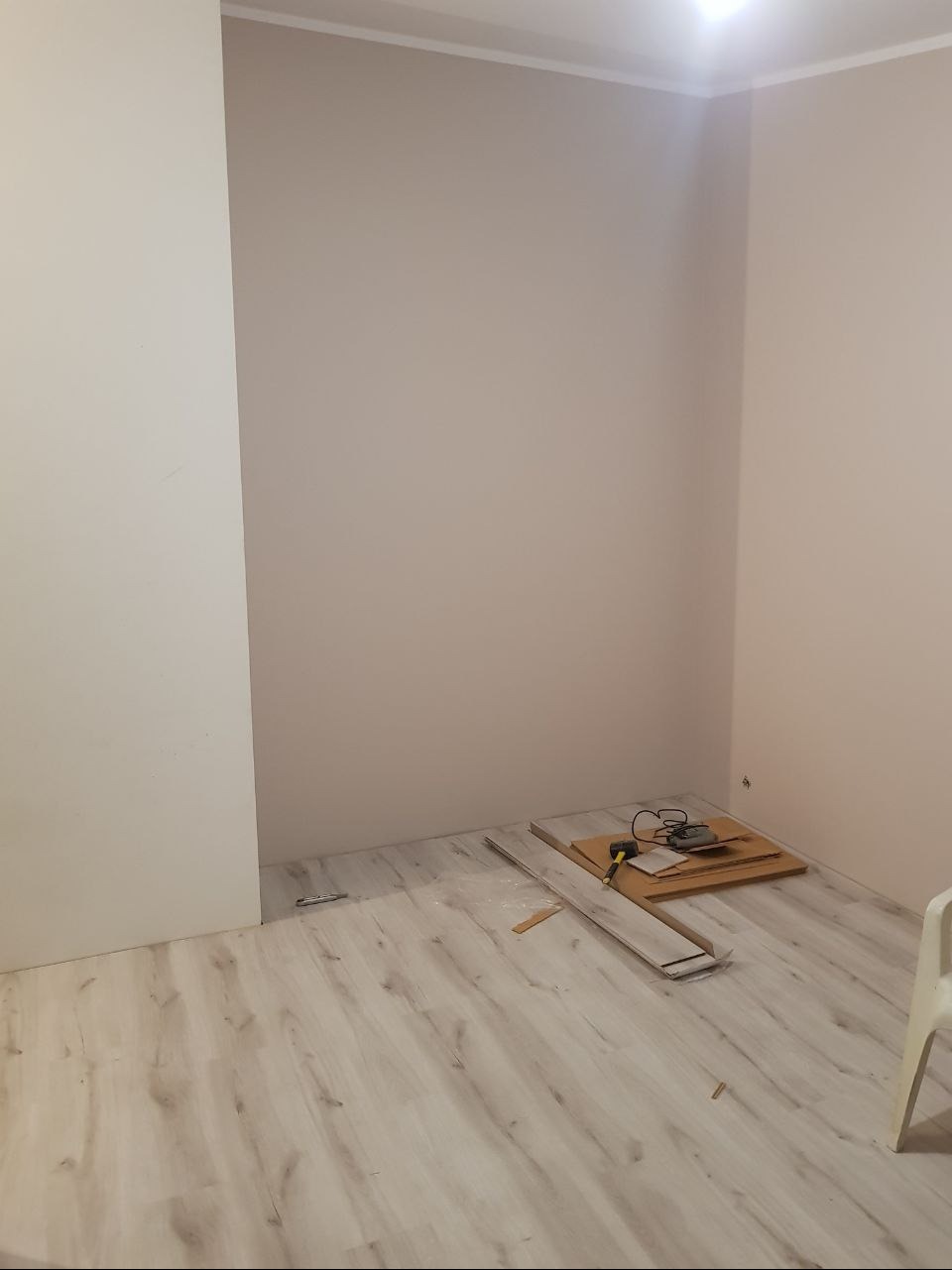 Pokój w trakcie prac wykończeniowych: ściany pomalowane na jasny beż, ułożona podłoga laminowana w odcieniach szarości, narzędzia i panele podłogowe leżące na podłodze.