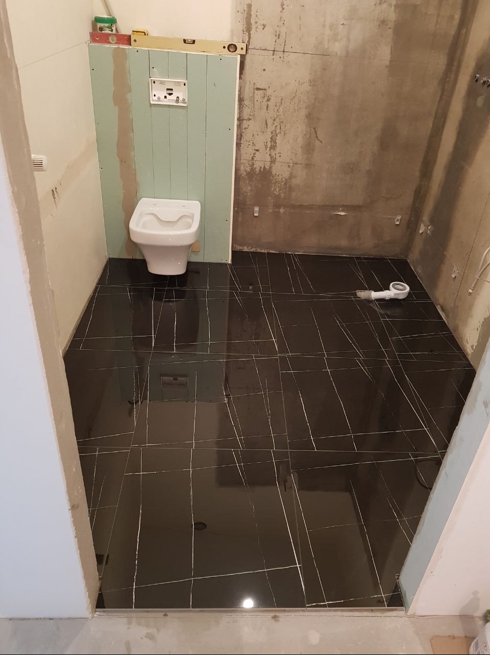 Montaż wiszącej toalety na tle płyty karton gips w łazience w trakcie remontu w Warszawie, widoczna czarna podłoga z białymi żyłkami.