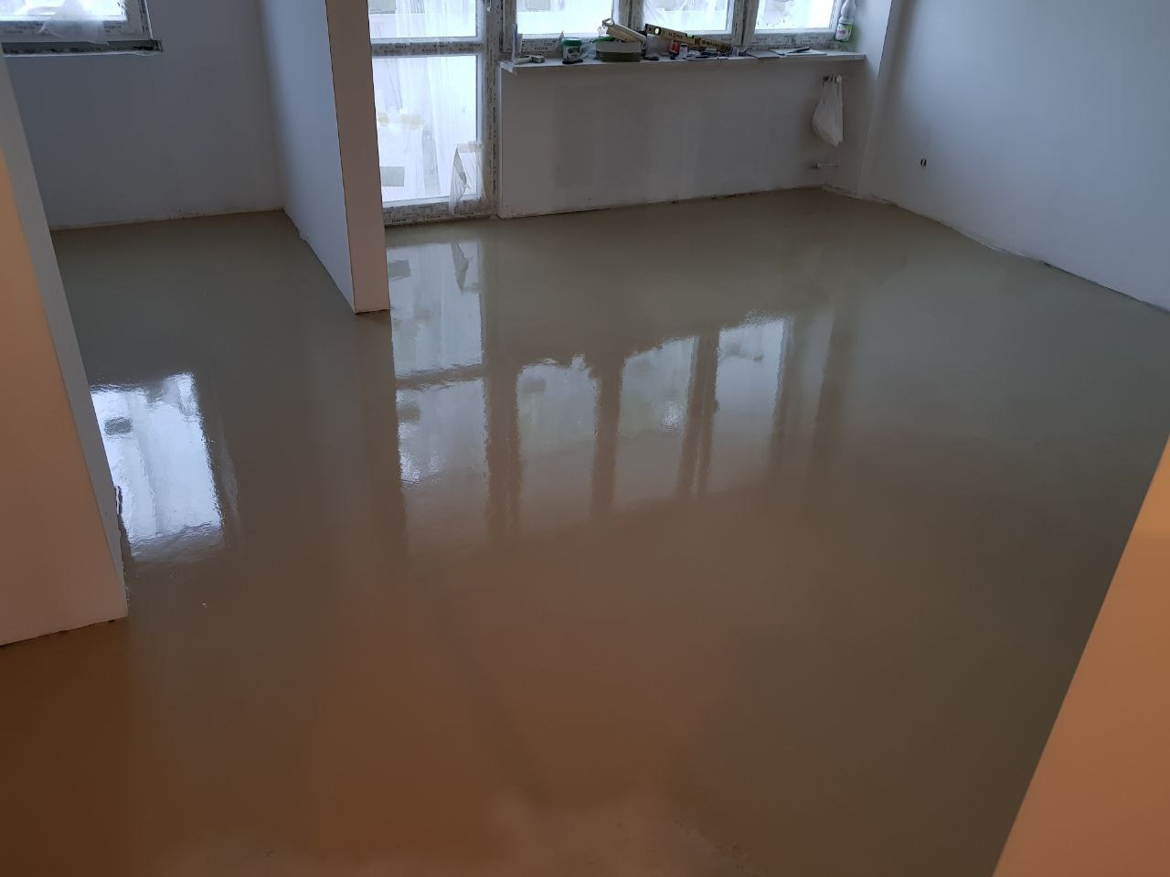 Wylany, samopoziomujący podkład podłogowy w jasnym odcieniu beżu, odbijający światło okien w pustym pokoju.