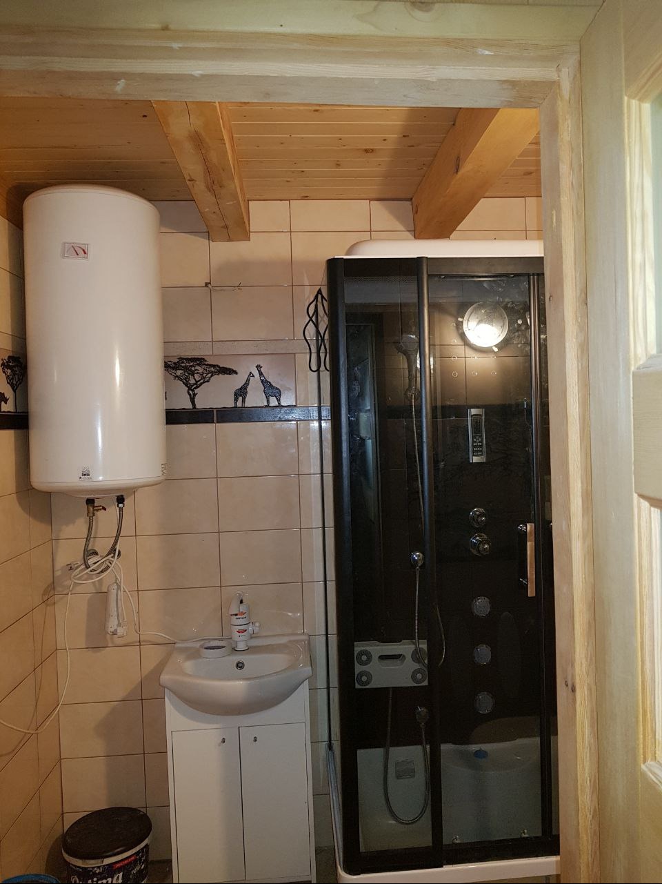 Wykończona łazienka z kabiną prysznicową z hydromasażem, bojlerem elektrycznym, umywalką z szafką i dekoracyjnymi płytkami z motywem afrykańskim.