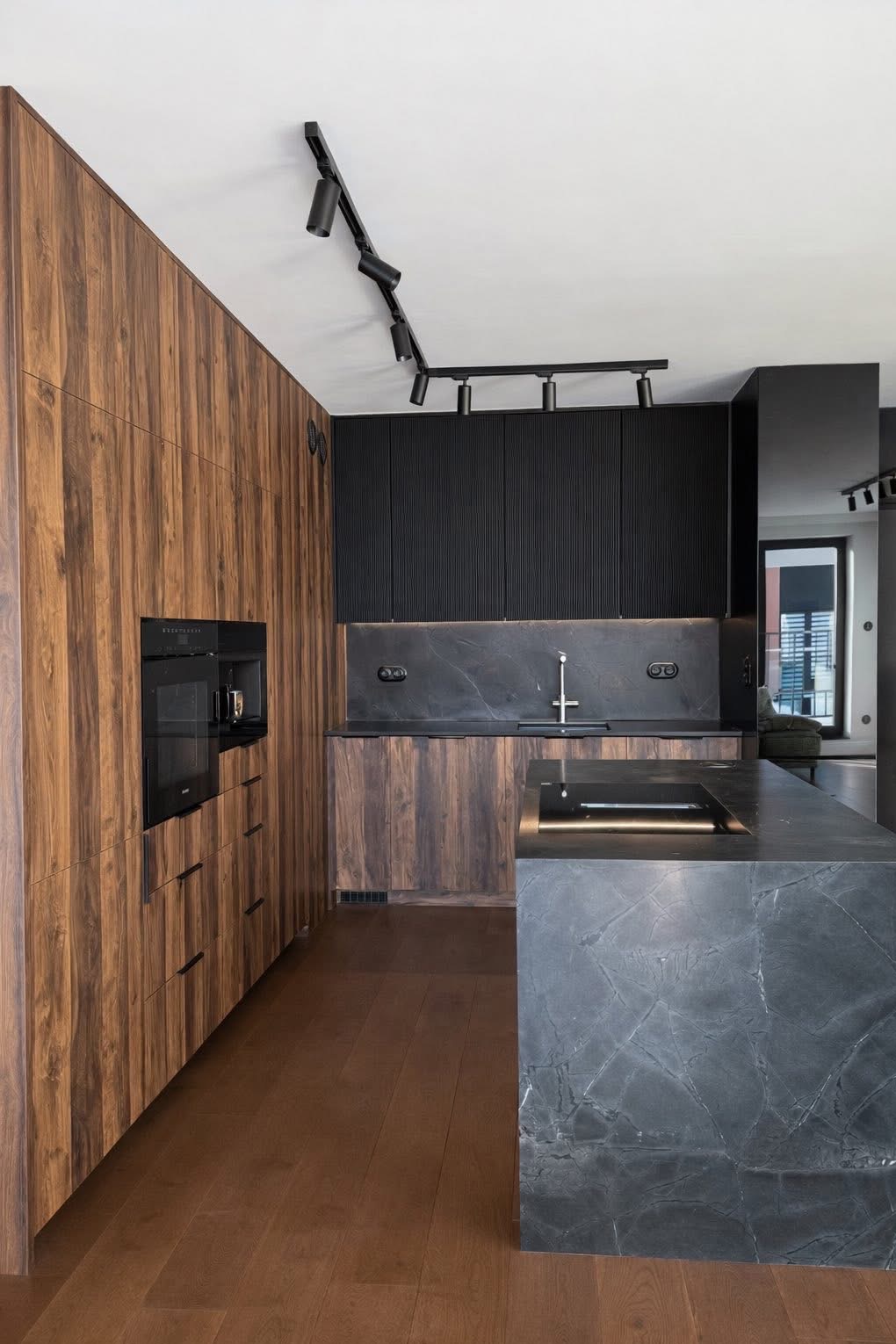 Nowoczesna kuchnia: drewniane fronty szafek, czarne ryflowane szafki wiszące, marmurowy blat wyspy, oświetlenie szynowe. Minimalistyczny design z dbałością o detale.