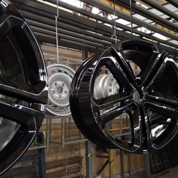 WOKA STAL WOJCIECH KALIKA - Błyszczące, czarne felgi samochodowe zawieszone na metalowym stelażu w hali produkcyjnej, prawdopodobnie tuż po procesie lakierowania.
