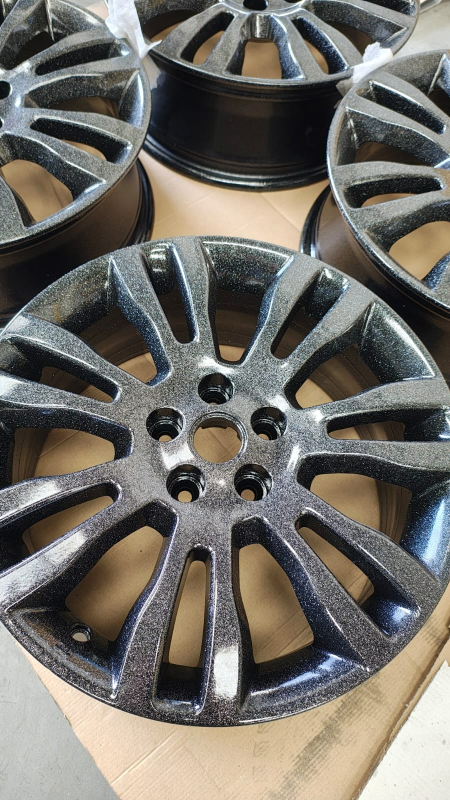 Felgi samochodowe po metalizacji natryskowej w kolorze czarnym z połyskującymi drobinkami, leżące na kartonie.