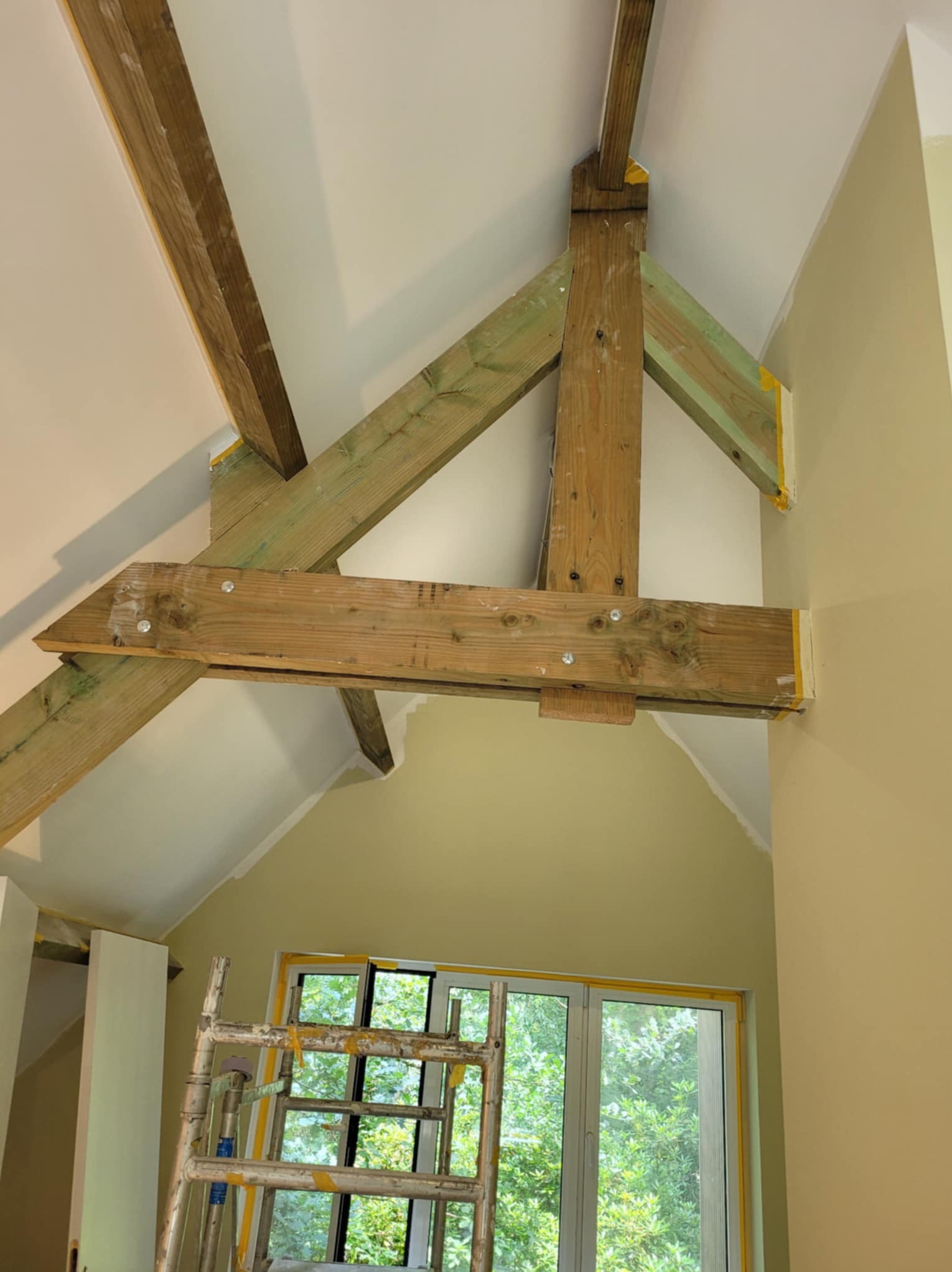 Drewniana konstrukcja stropu w trakcie prac w Świętochłowicach, zabezpieczona taśmą malarską, widoczny fragment rusztowania i okno.