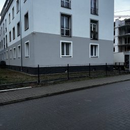 KORSAR Grzegorz Korczyński - Dwukondygnacyjny budynek z szarą dolną częścią elewacji i czarnym ogrodzeniem panelowym. W tle widoczna konstrukcja w trakcie budowy.