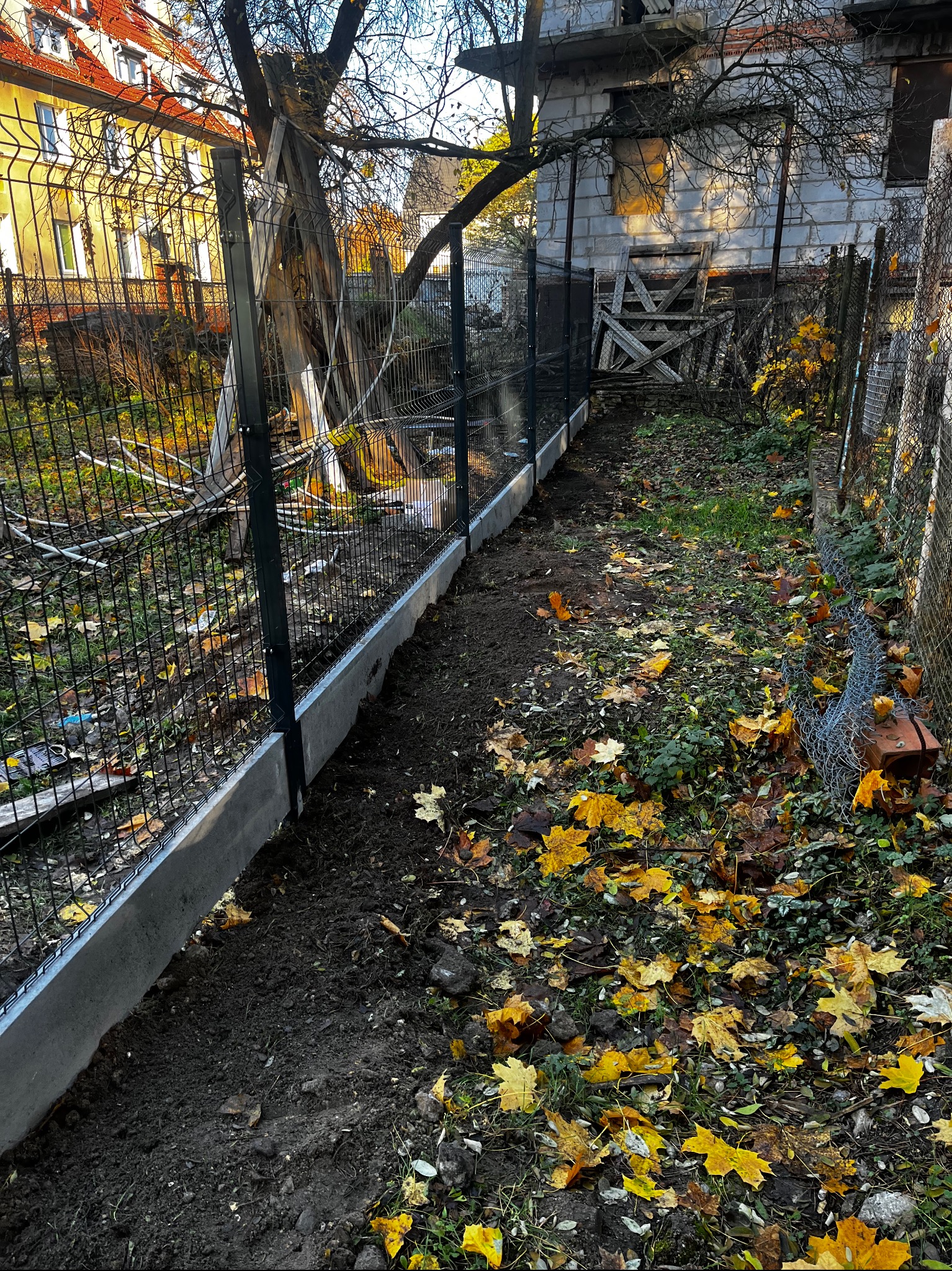 Nowoczesne ogrodzenie panelowe z podmurówką w Szczecinie, widok z perspektywy ziemi, jesienne liście na trawie. Solidna konstrukcja, estetyczne wykończenie.