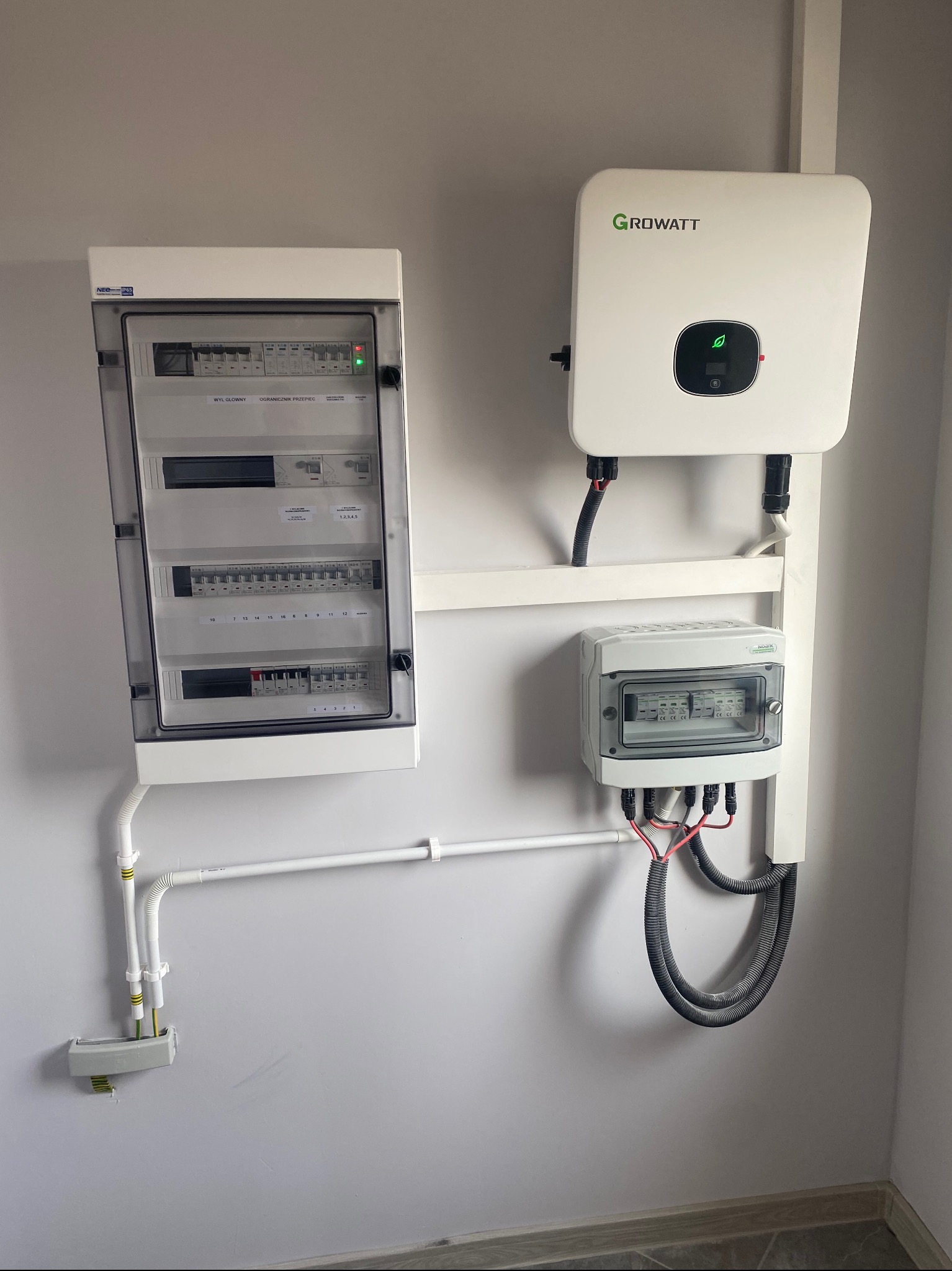 Instalacja fotowoltaiczna: rozdzielnice elektryczne i falownik Growatt zamontowane na ścianie wewnątrz budynku, widoczne okablowanie i zabezpieczenia.