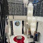 Eleganckie wnętrze z fotobudką: czerwony dywan prowadzi do okrągłej fotobudki z lustrzanym panelem, otoczonej dekoracyjnymi lampami i girlandami świetlnymi, w tle kryształowe żyrandole i balustrada.