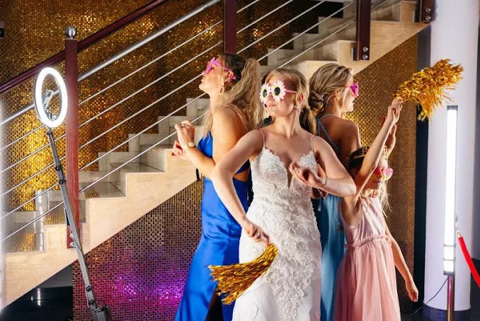 Grupa kobiet i dziewczynka w okularach pozują z rekwizytami przy ściance ze złotych płytek i oświetleniem LED.