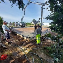 MSS MAREK WIĄCEK - Wylewka fundamentu domu jednorodzinnego z użyciem pompy do betonu. Widoczni pracownicy w trakcie wykonywania prac. Betonowa podstawa zbrojona siatką.