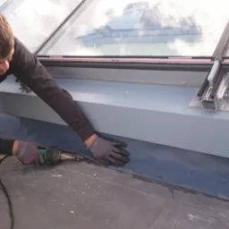 Pracownik w Grabówko uszczelnia dach płaski przy świetliku za pomocą zgrzewarki. Widoczne detale mocowania świetlika i membrana dachowa.