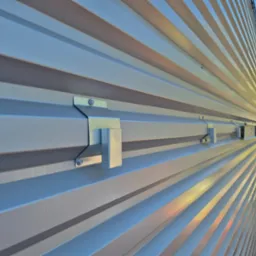 Szara, metalowa elewacja budynku z widocznymi mocowaniami. Ujęcie z boku, podkreślające rytmiczną strukturę paneli elewacyjnych i precyzję montażu.