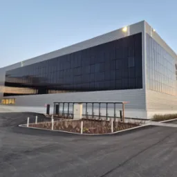 Nowoczesny budynek biurowy z panelami słonecznymi na elewacji, widok z parkingu. Szara fasada, geometryczny design, oświetlenie LED, minimalistyczna architektura.