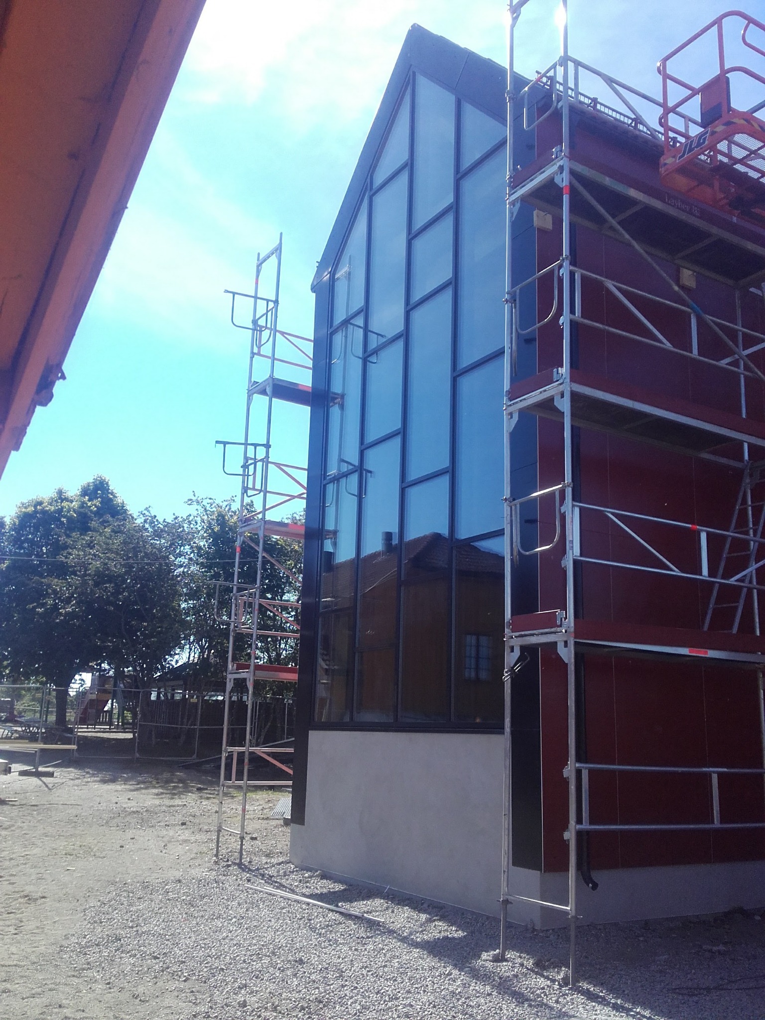 Budowa domu szkieletowego z dużymi oknami, widoczne rusztowania i teren budowy w słoneczny dzień. Dom w trakcie budowy.