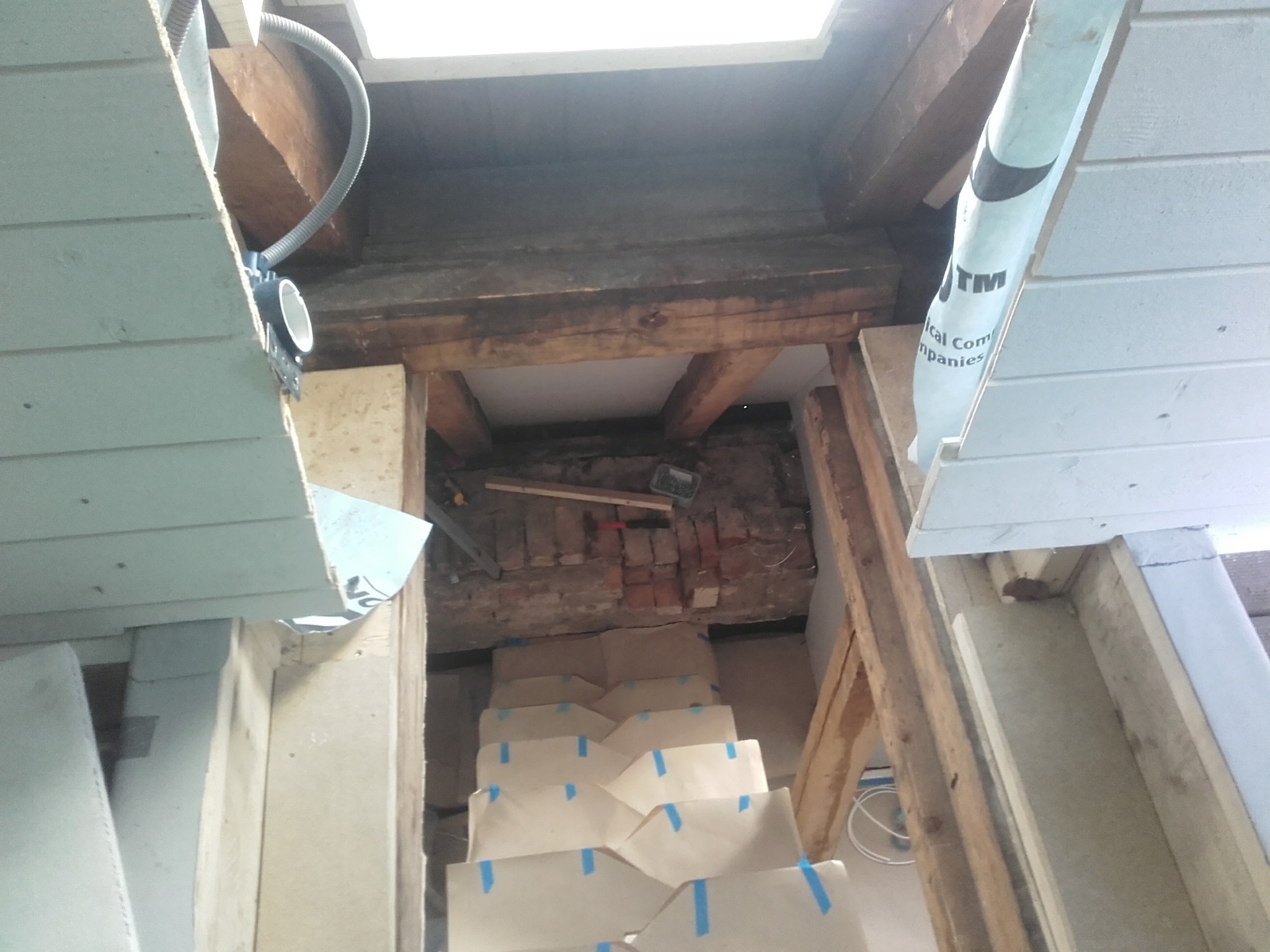 Poddasze w trakcie ocieplania: widoczne belki, izolacja, fragment muru z cegły i przygotowane schody z zabezpieczeniami. Prace wykończeniowe poddasza.