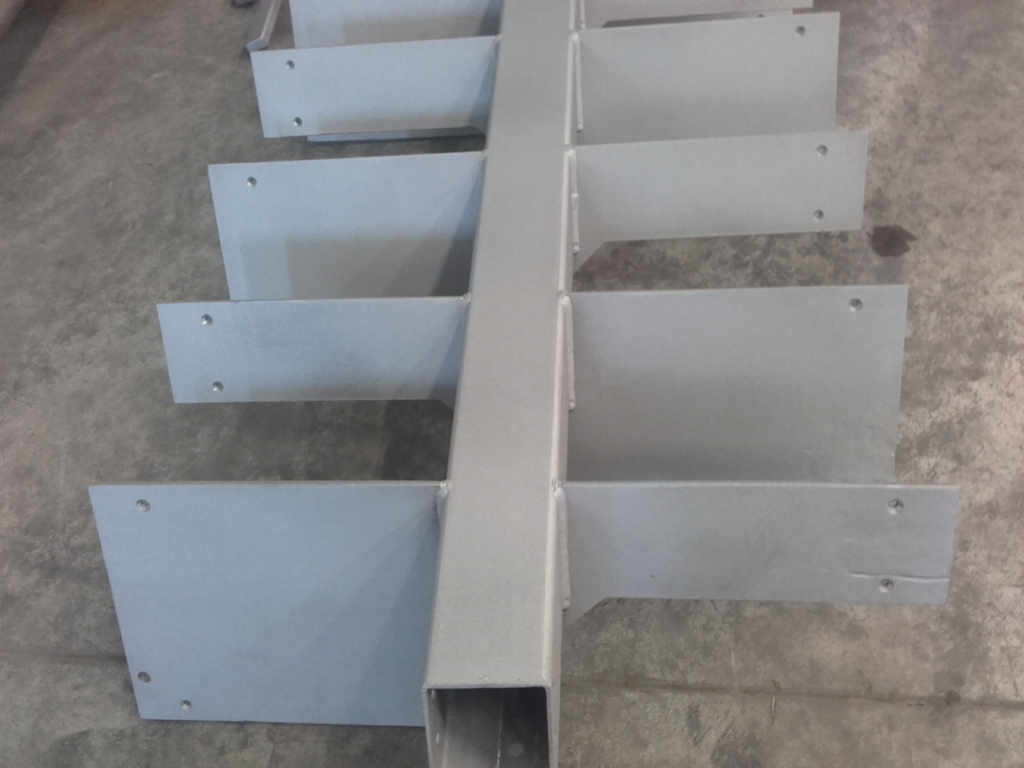 Metalowa konstrukcja z przyspawanymi płytkami, prawdopodobnie element obróbki blacharskiej, widoczne ślady spawania i otwory montażowe.