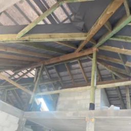 Konstrukcja drewniana poddasza z widoczną membraną dachową przed ociepleniem, jasne drewno impregnowane na zielono, fragment ściany z betonu komórkowego.