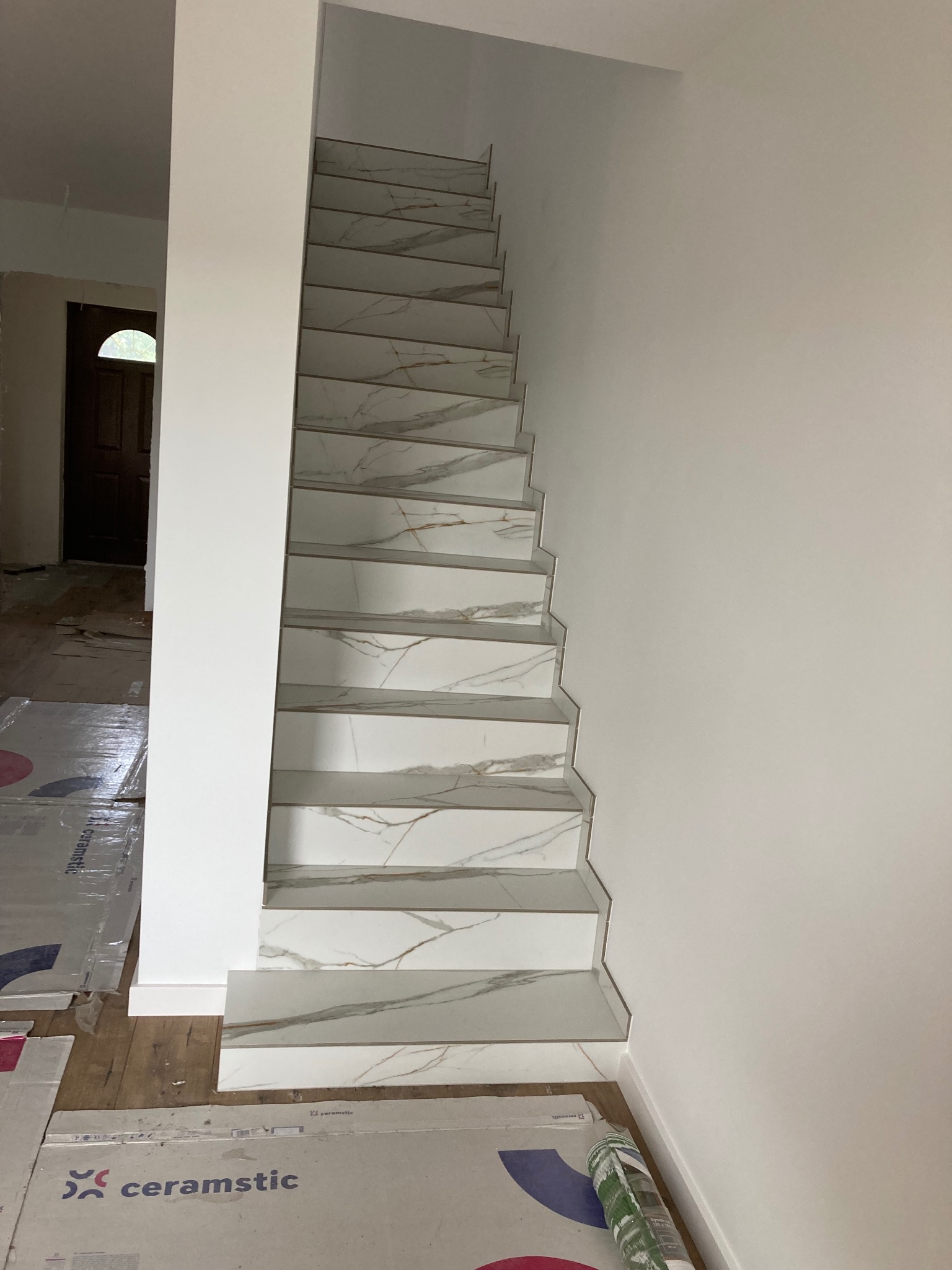Schody wyłożone płytkami imitującymi marmur, z widocznymi fugami i zabezpieczeniem podłogi kartonem oraz tubą silikonu.