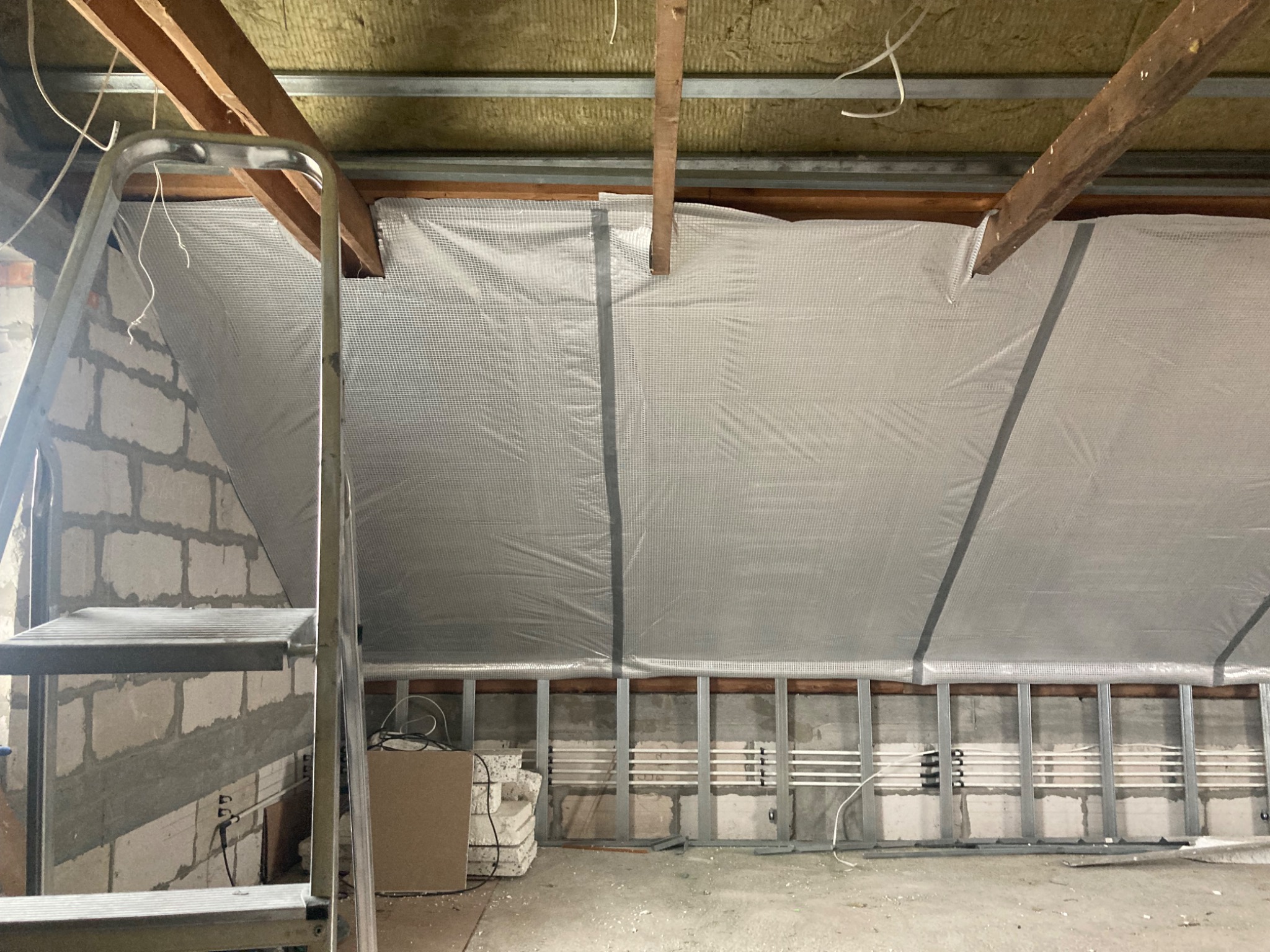 Poddasze w Bobrownikach w trakcie ocieplania, widoczne wełna mineralna, folia paroizolacyjna, metalowa konstrukcja i drabina.
