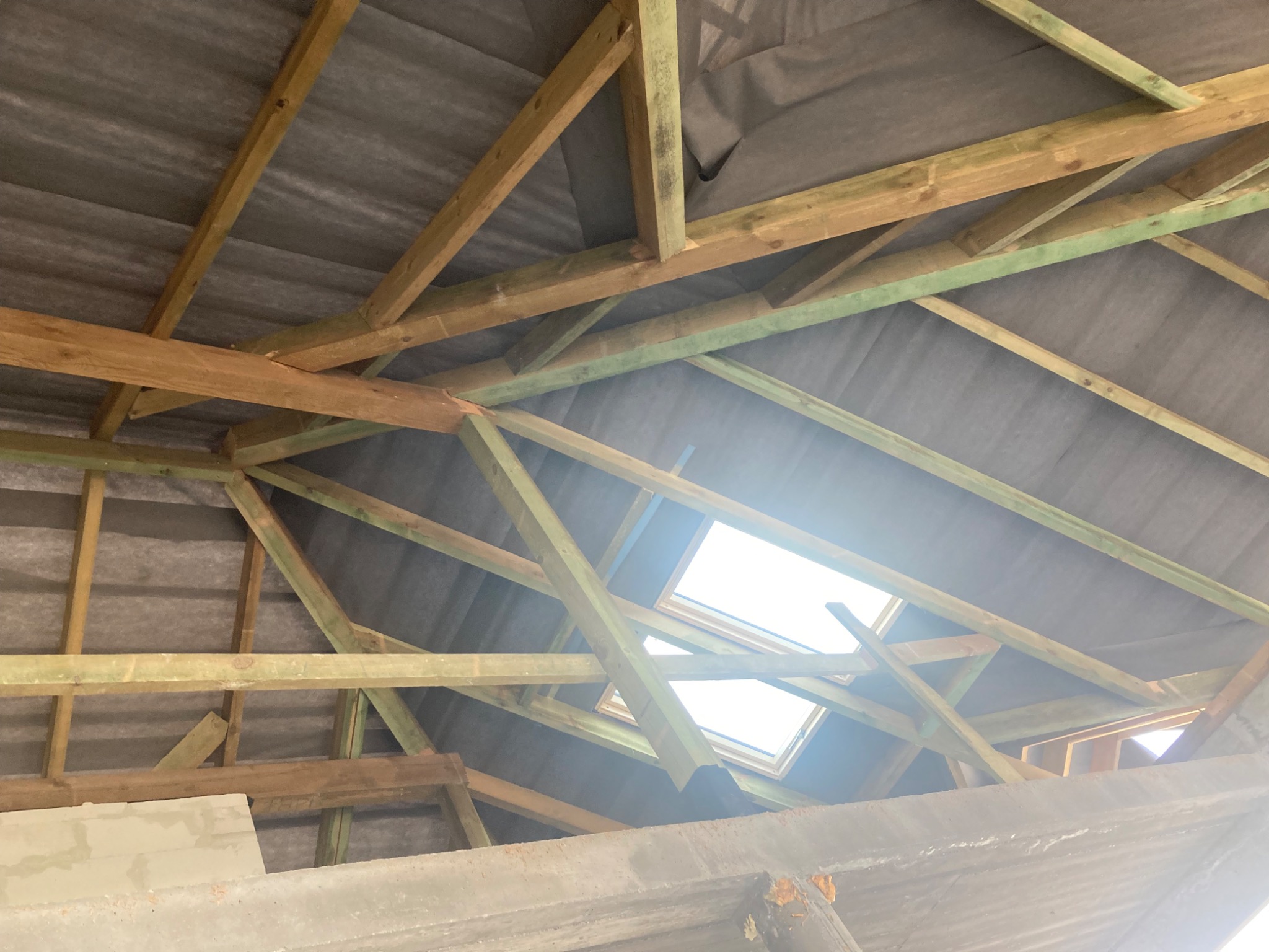Konstrukcja drewniana poddasza z widocznymi łatami, kontrłatami i membraną dachową, przygotowana pod ocieplenie, z oknami dachowymi w tle.