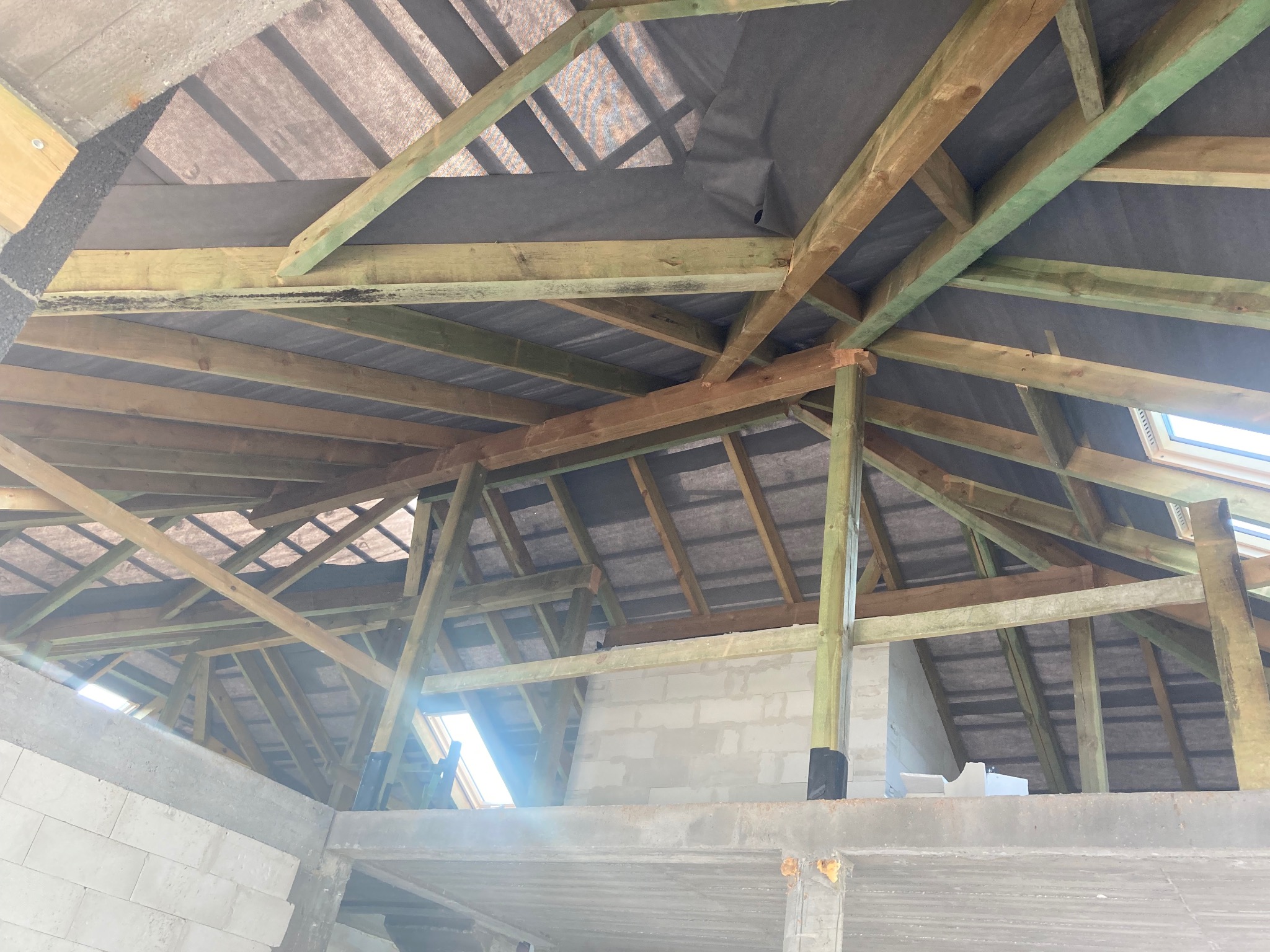 Konstrukcja drewniana poddasza z widoczną membraną dachową przed ociepleniem, jasne drewno impregnowane na zielono, fragment ściany z betonu komórkowego.