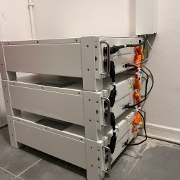 Ciepła Energia - Trzy moduły bateryjne litowo-jonowe SE-G5.1 Pro-B ustawione jeden na drugim, z widocznymi kablami zasilającymi i komunikacyjnymi, umieszczone w pomieszczeniu o minimalistycznym wystroju.