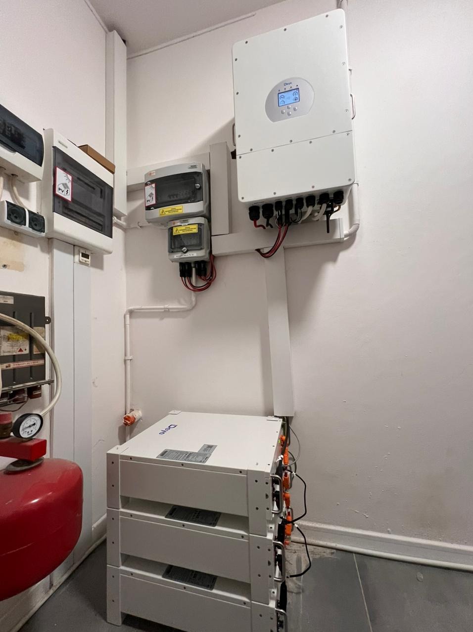 Trzy moduły magazynu energii ułożone jeden na drugim, z podłączonym inwerterem i zabezpieczeniami elektrycznymi na ścianie w pomieszczeniu technicznym.