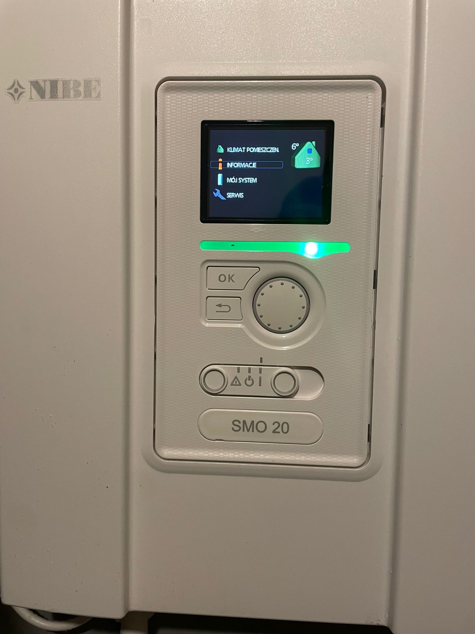 Panel sterowania pompy ciepła Nibe SMO 20 z podświetlonym ekranem, wyświetlającym temperaturę pomieszczenia i opcje menu. Widoczny interfejs użytkownika.