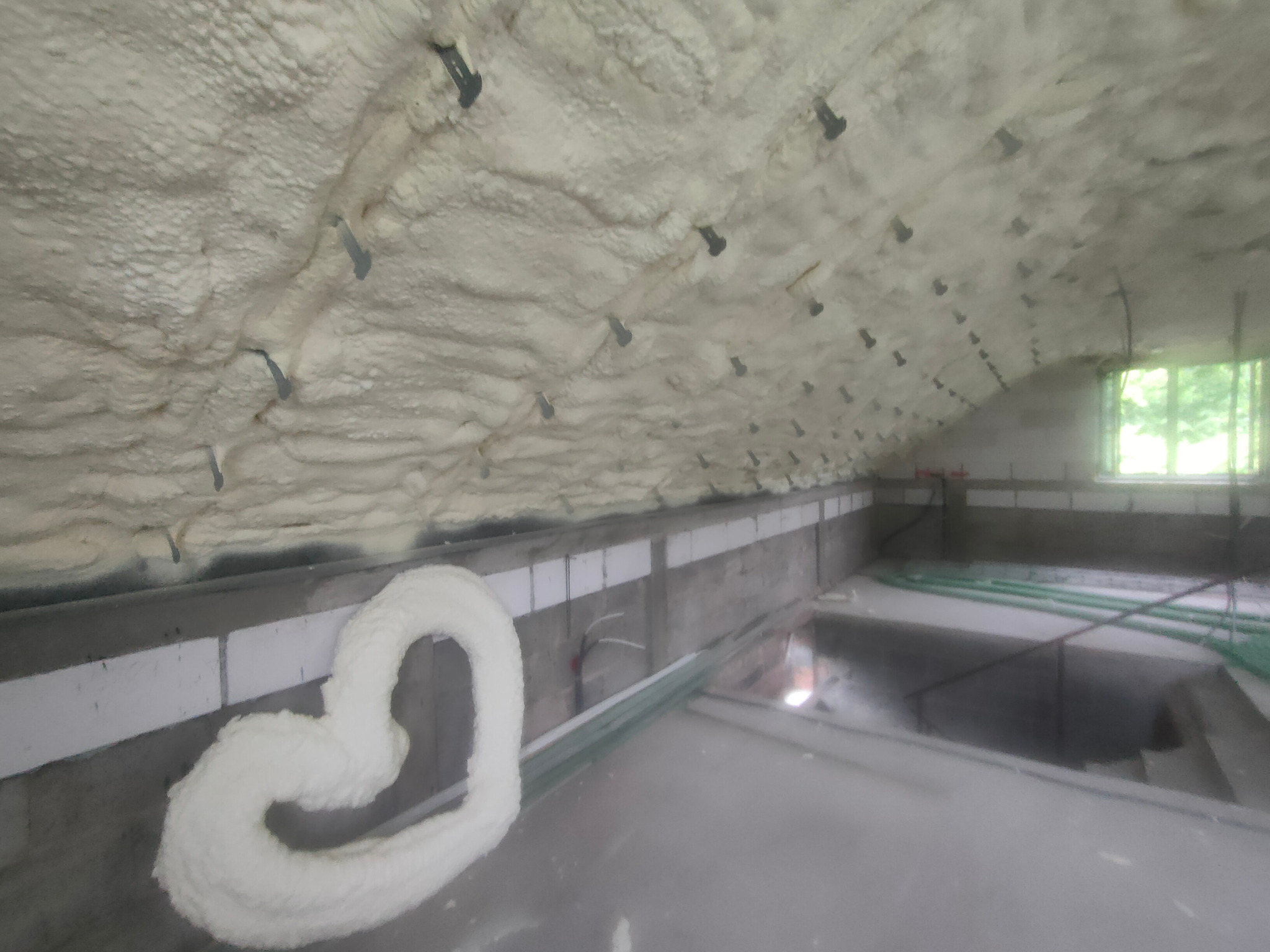 Poddasze z ociepleniem pianką PUR, widoczne mocowania i kształt serca z pianki na ścianie. Okno w tle. Nietypowe ujęcie, ukazujące detale izolacji.