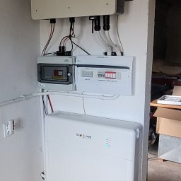 AM GROUP SOLAR MARCIN SERKOWSKI - Biały magazyn energii Sofar połączony z inwerterem i rozdzielnicami na ścianie w surowym pomieszczeniu.