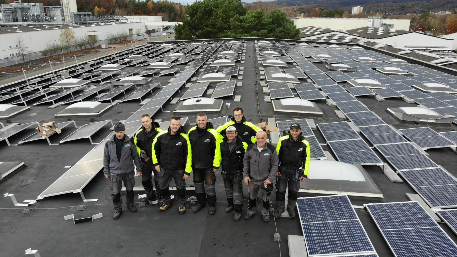 Grupa monterów w odzieży roboczej na dachu budynku z zainstalowanymi panelami słonecznymi, widok z góry.