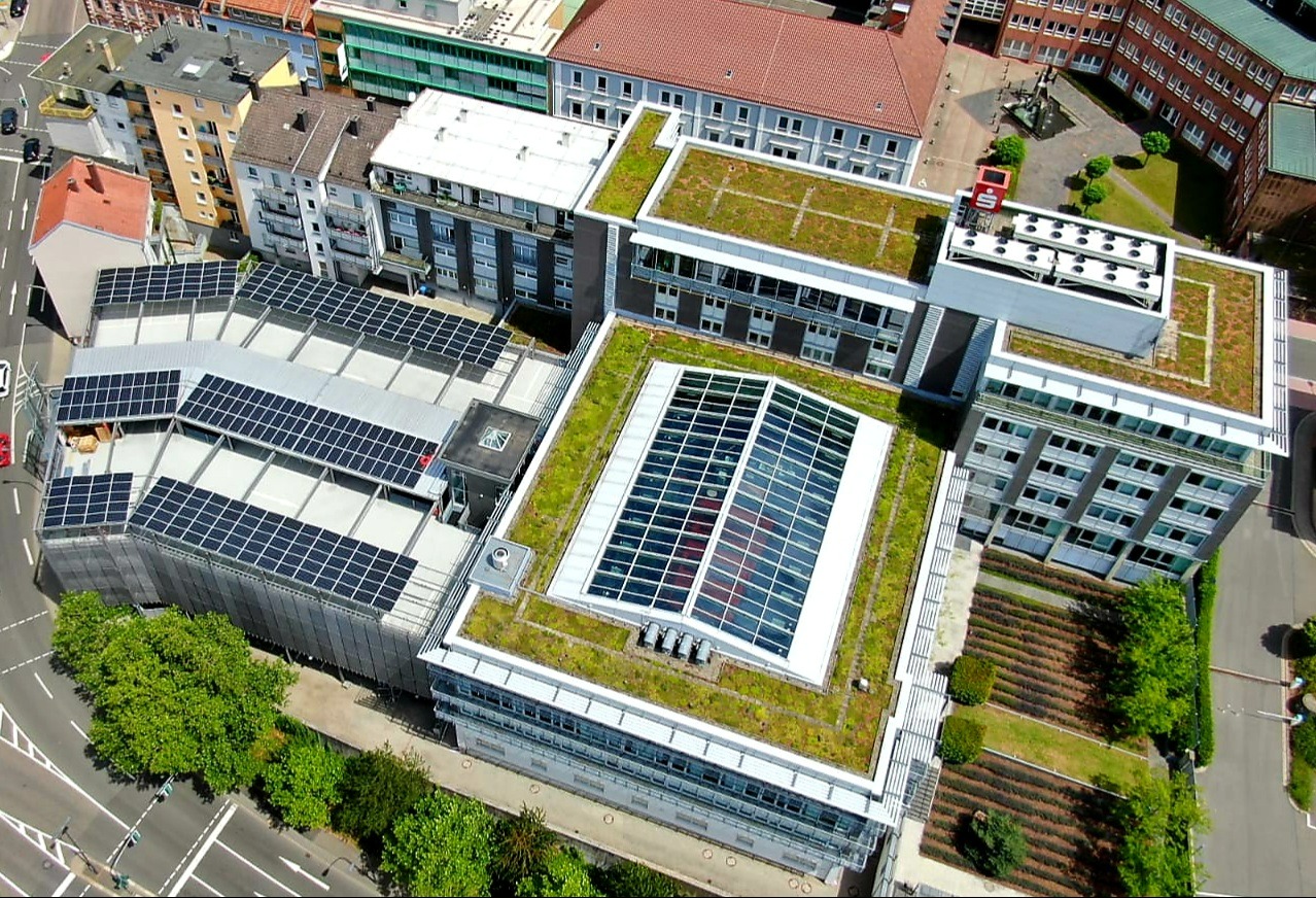 Widok z góry na budynek biurowy z panelami słonecznymi na dachu parkingu i zielonymi dachami.