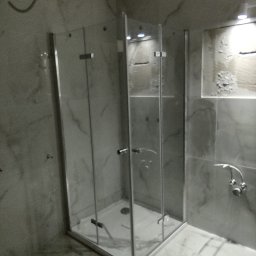 Michał Gwizdek - Nowa, narożna kabina prysznicowa z transparentnego szkła, zamontowana w łazience wyłożonej szarymi płytkami imitującymi marmur, widoczny odpływ liniowy w brodziku.