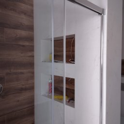 Michał Gwizdek - Nowoczesna kabina prysznicowa z przesuwnymi drzwiami, drewnopodobne płytki na ścianie, wnęki z akcesoriami i narzędziami.