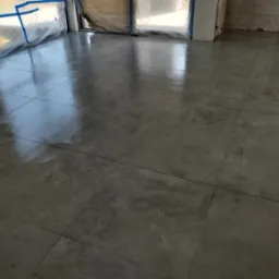 Świeżo ułożona, lśniąca, szara podłoga z płytek w pomieszczeniu w trakcie remontu, z oknami zabezpieczonymi folią ochronną.