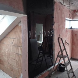 Michał Gwizdek - Montaż lustrzanej ściany w łazience w trakcie remontu, widoczne klamerki mocujące, drabina i surowe ściany przygotowane do wykończenia.