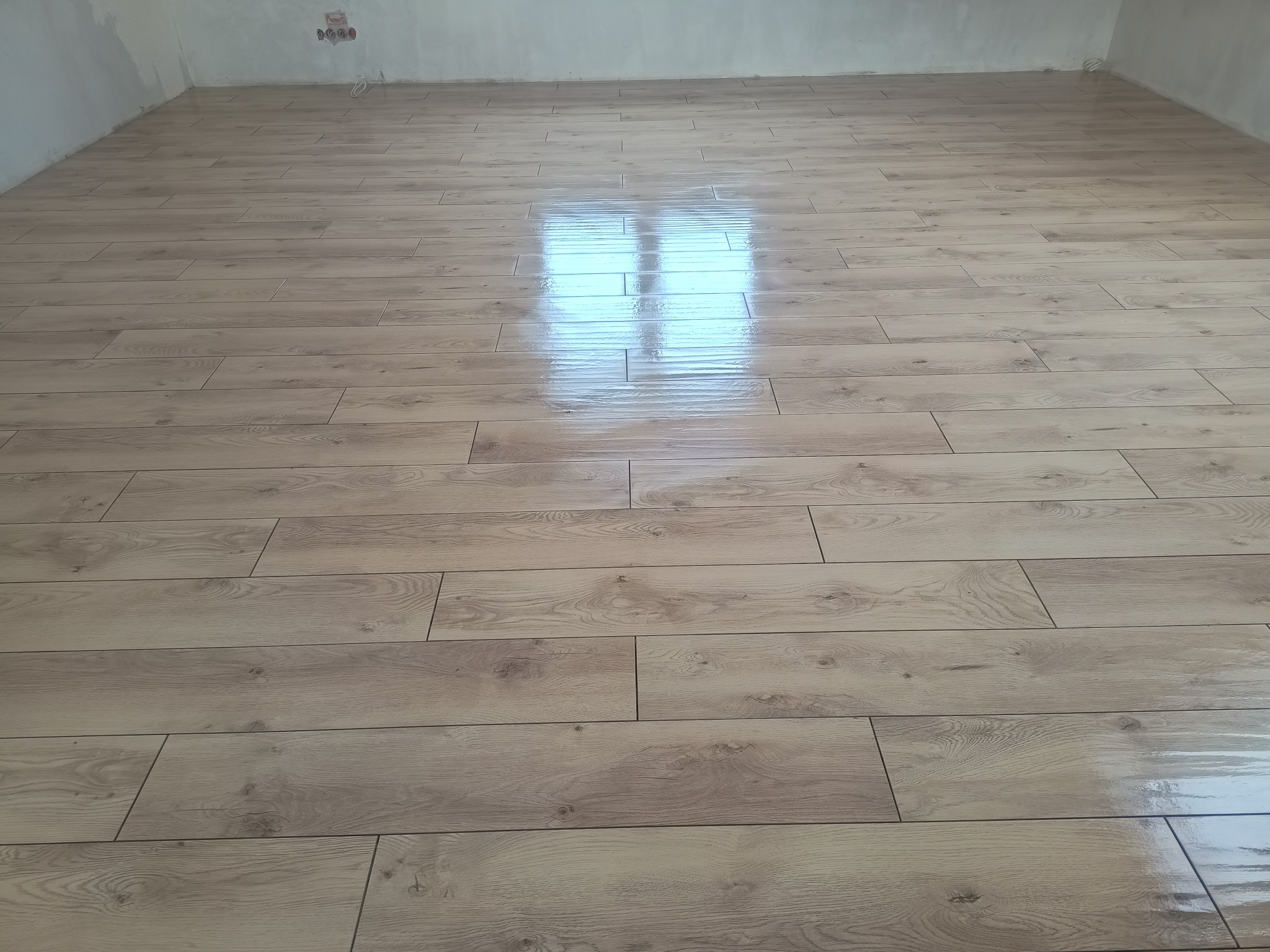 Ułożona podłoga z paneli imitujących drewno, z widocznym odbiciem światła okiennego, świeżo po montażu w surowym wnętrzu.