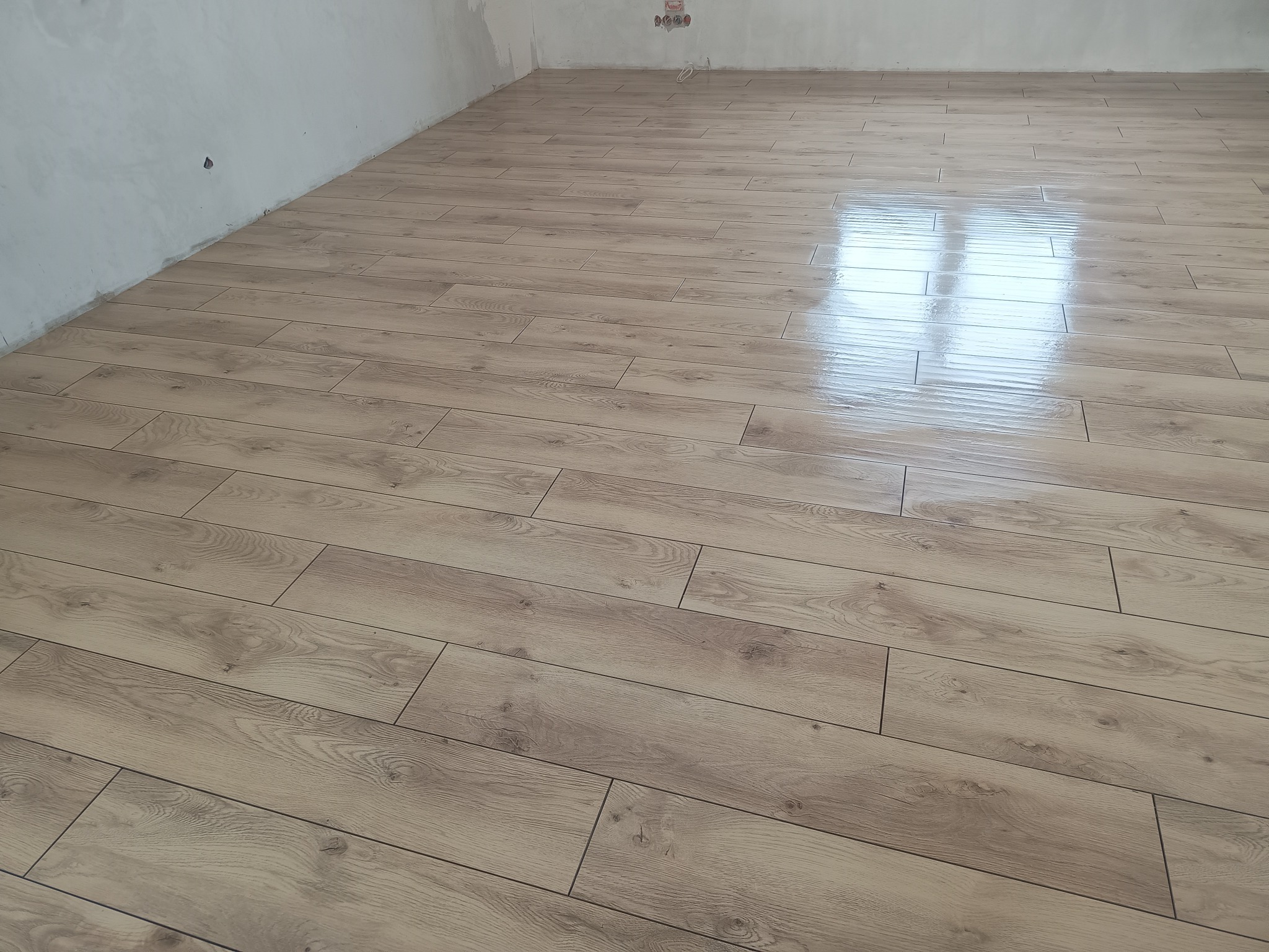 Jasne panele podłogowe z wyraźną strukturą drewna, ułożone w nowym pomieszczeniu z surowymi ścianami, odbijające światło okna.